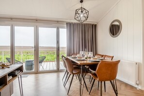 Un coin repas avec une table dressée pour quatre personnes, de grandes fenêtres et une vue sur la verdure environnante.