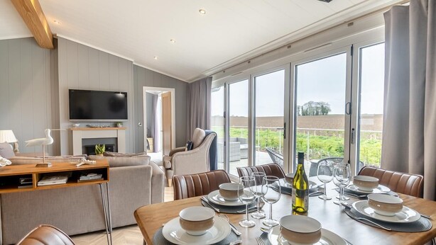 Een moderne eetruimte met een tafel voor zes personen, een televisie in de woonkamer en grote ramen met uitzicht op de omgeving.
