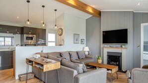 Een moderne woonkamer met een grijze bank, een houten salontafel en een flatscreen televisie boven een open haard.