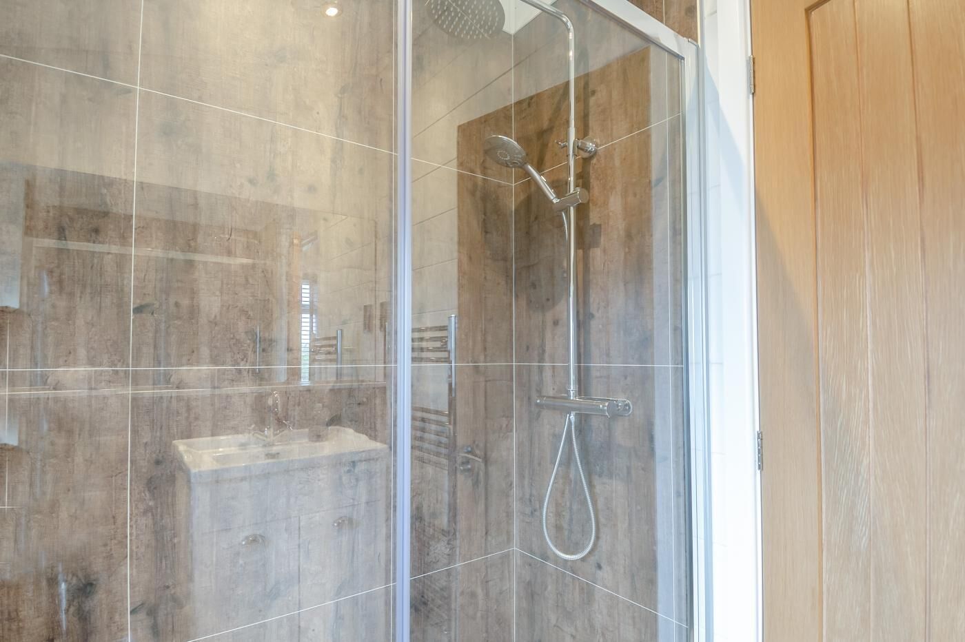 Une douche moderne dotée d’un pare-douche en verre, d’un pommeau de douche à main et d’un robinet à main.