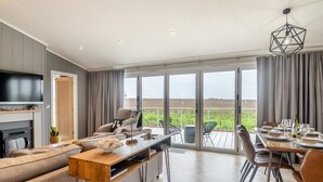 Een ruime woonkamer met een grote televisie, bank en een eethoek, met uitzicht op het landschap.
