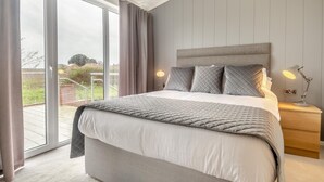 Een slaapkamer met een groot bed, een nachtkastje met een lamp en uitzicht op het landschap door een schuifdeur.