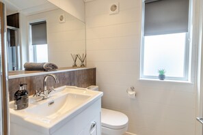Une salle de bain moderne avec un lavabo blanc, un miroir et des toilettes. Il y a une fenêtre avec une plante posée sur le rebord.