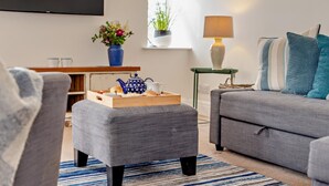 A modern living room with a grey sofa, a matching ottoman, a wooden coffee table, a blue teapot, and a potted plant. - 3 Bed in Treknow (oc-h29194) (Treknow)