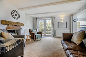 Un salon avec une cheminée, un mur en pierre, une grande fenêtre et une horloge au mur.