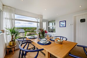 Un coin repas avec une table dressée pour deux personnes, des chaises, une plante en pot et une vue sur la campagne.