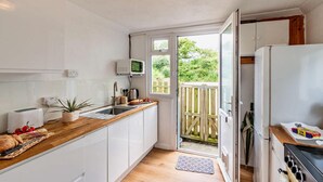 A compact kitchen with white cabinets, a wooden countertop, a built-in microwave, a sink, and a stove. - 2 Bed in St. Dogmaels (oc-s29213) (Saint Dogmaels)