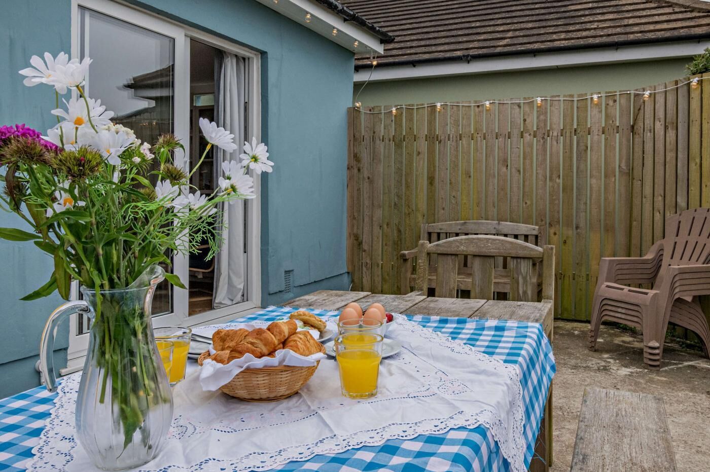 A patio with a table set for breakfast, including croissants, eggs, and orange juice.