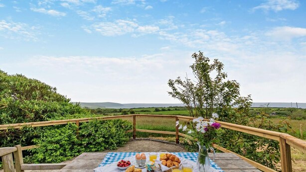 A picnic setup with a checkered tablecloth, food, and drinks on a wooden deck with a view of the countryside. - 2 Bed in St. Dogmaels (oc-s29213) (Saint Dogmaels)