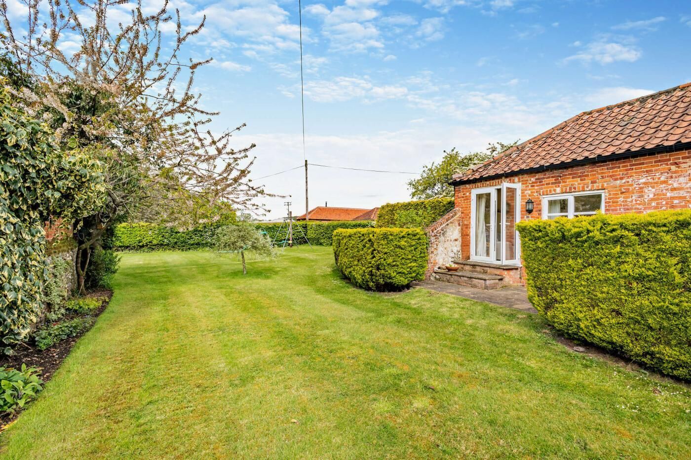 A well-maintained garden with a lawn, a brick house with a tiled roof, and neatly trimmed hedges.