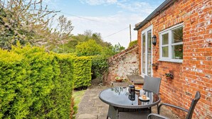 A brick house with a glass door, a small patio with a table and chairs, and a well-maintained hedge. - 1 Bed in Barton Turf (oc-s29126) (Neatishead)