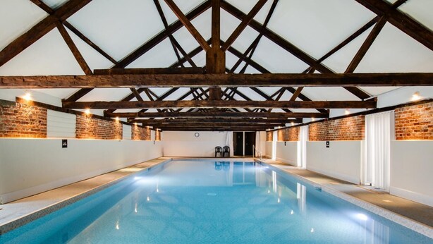 An indoor swimming pool with a high ceiling and exposed wooden beams, surrounded by brick walls and white panels. - 1 Bed in Barton Turf (oc-s29126) (Neatishead)