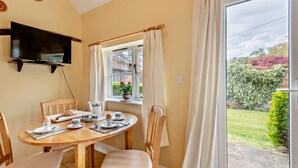 A dining area with a table set for breakfast, a television mounted on the wall, and a window with curtains. - 1 Bed in Barton Turf (oc-s29126) (Neatishead)
