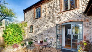 A stone building with a patio area featuring a table and chairs, a wooden fence, and a variety of plants. - 3 Bed in Weybourne (oc-t29167) (Weybourne)