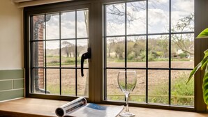 A window with a view of a rural landscape, a rolled-up newspaper, and a wine glass on the windowsill. - 3 Bed in Weybourne (oc-t29167) (Weybourne)