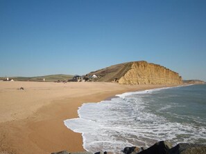 A coastal beach with a prominent cliff, sandy shore, and a few buildings in the background. - 2 Bed in West Bay (oc-m29216) (West Bay)