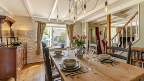 Een eetkamer met een houten tafel voor vier personen, een bloemenvaas en een trap naar een ander niveau.