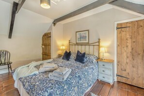 Een slaapkamer met een bed, twee nachtkastjes, een stoel, een houten kledingkast en een schilderij aan de muur.
