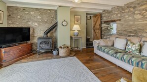 Een gezellige woonkamer met een stenen muur, een televisie, een open haard en een bank.