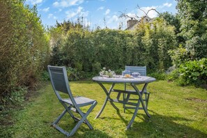 Een tuin met een ronde tafel en twee stoelen, omringd door groen.