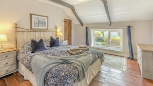Een slaapkamer met een bed, nachtkastjes, een raam en uitzicht op groen.