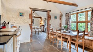 Una cucina rustica con pavimento in pietra, travi in legno e zona pranzo con parete in mattoni e ampie finestre.