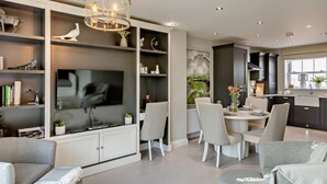Uma sala de estar moderna com televisão de tela plana, área de jantar com mesa e cadeiras, e cozinha com armários escuros.