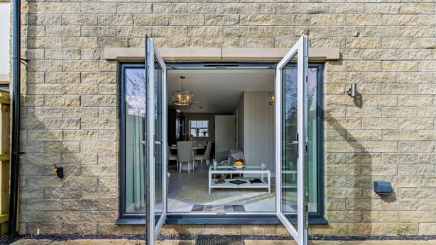 Uma casa moderna com fachada de pedra, porta de vidro que dá para uma sala de jantar com mesa e cadeiras, e cozinha visível ao fundo.