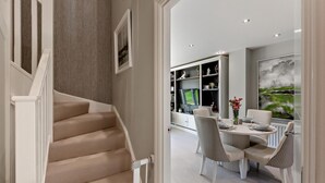 Um interior moderno com escada, área de refeições e uma grande janela com obras de arte.