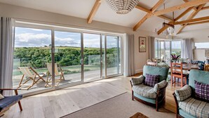A spacious room with large sliding glass doors leading to a scenic outdoor view, wooden beams on the ceiling, and a dining area with a table and chairs.