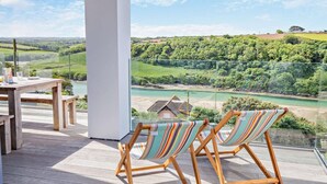 A balcony with wooden furniture and a view of a river and green landscape.