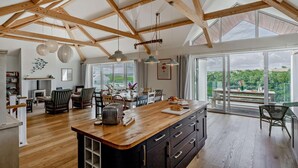 A spacious kitchen with a large island, wooden beams, and large windows offering a view of the outdoors.