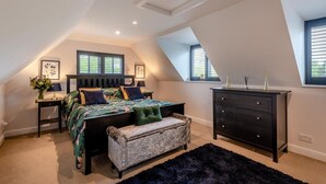 A bedroom with a sloped ceiling, a bed with a quilted bedspread, a bench, a dresser, and two bedside tables with lamps. - 1 Bed in Pluckley (oc-a29239) (Smarden)