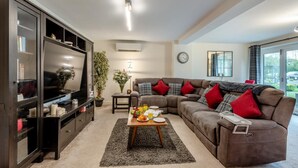 A modern living room with a sectional sofa, a flat-screen TV, a coffee table with snacks, and a large window offering a view of the outdoors. - 1 Bed in Pluckley (oc-a29239) (Smarden)