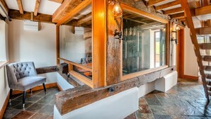 A rustic interior with exposed wooden beams, a large window, a cushioned bench, and a chair. - 4 Bed in Heywood (oc-t29040) (Westbury)