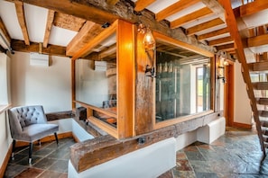 A rustic interior with exposed wooden beams, a large window, a cushioned bench, and a chair. - 4 Bed in Heywood (oc-t29040) (Westbury)
