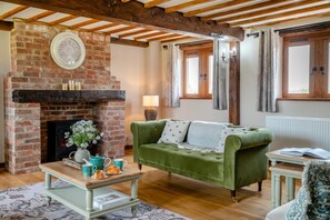 A cozy living room with a brick fireplace, a green sofa, a wooden coffee table, and a window with curtains. - 4 Bed in Heywood (oc-t29040) (Westbury)