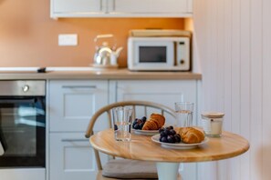 A kitchen with a microwave, kettle, and oven. There's a table with croissants, blueberries, a glass of water, and a candle. - 1 Bed in Craven Arms (oc-o29275) (Craven Arms)