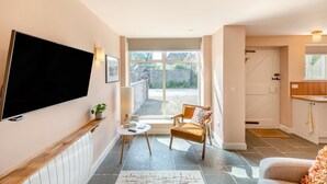 Una sala de estar moderna con un televisor de pantalla plana, un sillón cómodo, una mesita pequeña y un ventanal que ofrece vistas al exterior.