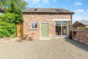 A small brick building with a green door, a window, and a patio with a table and chairs. - 1 Bed in Craven Arms (oc-o29275) (Craven Arms)