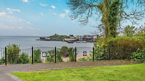 A coastal view with a grassy area, a metal fence, and buildings across the water. - 1 Bed in Tenby (oc-p29296) (Tenby)