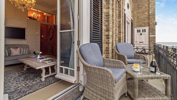 Un balcon agrémenté de meubles en osier, une table avec des livres et un lustre.