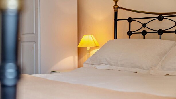 A bed with a headboard, a bedside table with a lamp, and a wall with a door. - 2 Bed in St. Issey (oc-t29235) (Saint Issey)