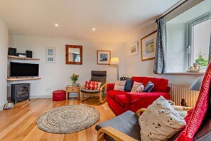 A cozy living room with a red sofa, a wooden chair, a TV, a fireplace, and a window with curtains. - 2 Bed in St. Issey (oc-t29235) (Saint Issey)