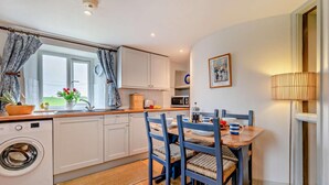 A compact kitchen with a washing machine, a dining table with chairs, and a microwave. - 2 Bed in St. Issey (oc-t29235) (Saint Issey)