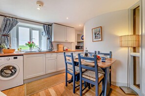 A compact kitchen with a washing machine, a dining table with chairs, and a microwave. - 2 Bed in St. Issey (oc-t29235) (Saint Issey)