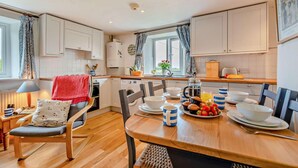 A modern kitchen with white cabinets, a dining table set with plates, cups, and a fruit bowl. - 2 Bed in St. Issey (oc-t29235) (Saint Issey)