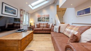 A spacious living room with a high ceiling, a wooden coffee table, a brown sofa set, and a skylight. - 3 Bed in Freshwater East (oc-w29240) (Freshwater East)