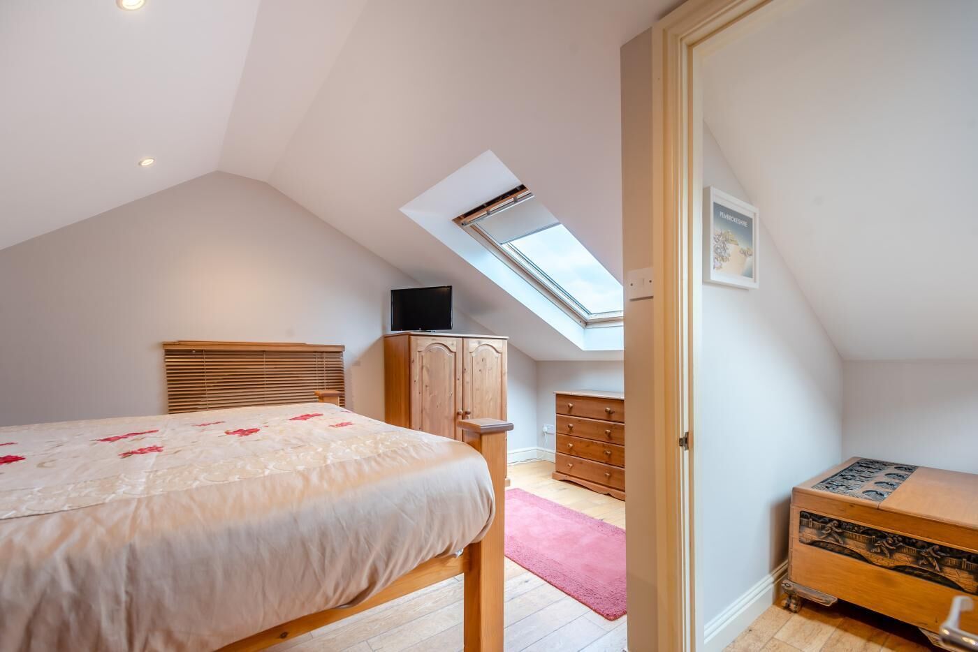 Un dormitorio con cama, armario de madera y tragaluz.