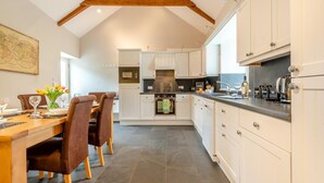 A modern kitchen with white cabinets, a dining area with a wooden table and chairs, and a large window providing natural light. - 3 Bed in Freshwater East (oc-w29240) (Freshwater East)